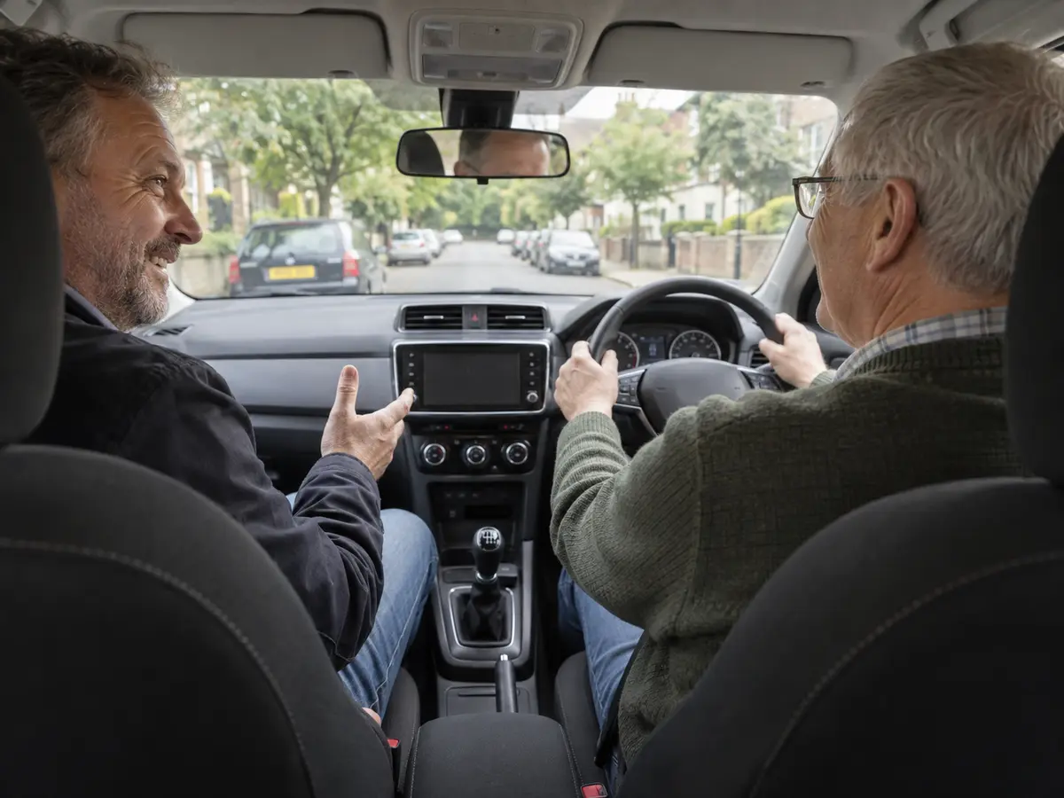 A mature adult student driving while a calm instructor chats with them.